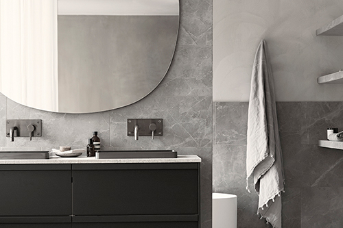 Badrum med ljusgrå sten och svart kommod och en stor spegel