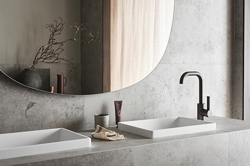 Detaljbild av ett badrum med ljusgrå sten, spegel och handfat