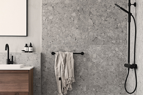Badrum med grå sten, svart dusch och träkommod